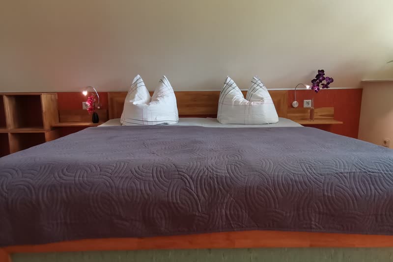 Doppelbett mit Holzrahmen, dunkler Tagesdecke und Regal unter der Dachschräge