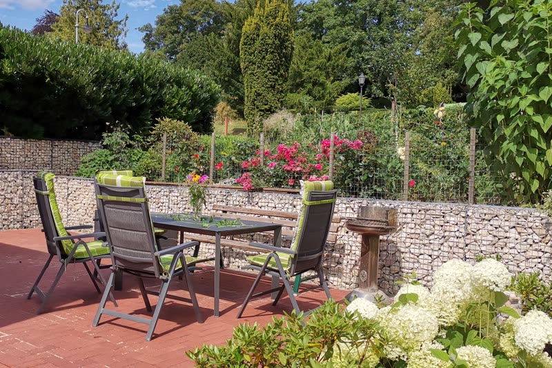 Terrasse mit Sitzgruppe und Blumenbeeten vor einer Steinmauer im Garten