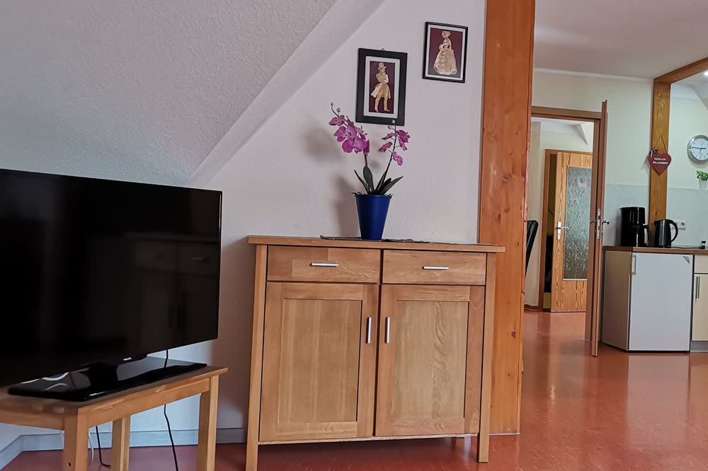 Heller Wohnbereich mit Fernseher, Sideboard und Blick in die offene Küche unter der Dachschräge